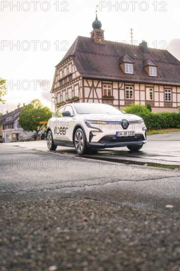 A white electric car parked in front of a traditional building with a bell tower in an old town, Deer E, car sharing, electric car, Calw, Black Forest