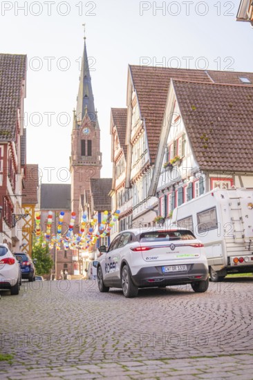 A car drives in an old town with colourful garlands in front of a church, Deer E, car sharing, electric car, Calw, Black Forest
