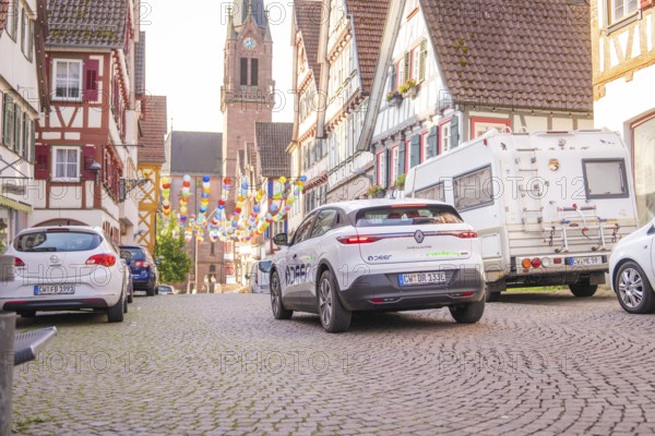 Cars parked in an old town, decorated with colourful garlands and a church in the background, Deer E, car sharing, electric car, Calw, Black Forest