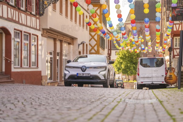 White car in an alley decorated with colourful lanterns under a blue sky, Deer E, car sharing, electric car, Calw, Black Forest