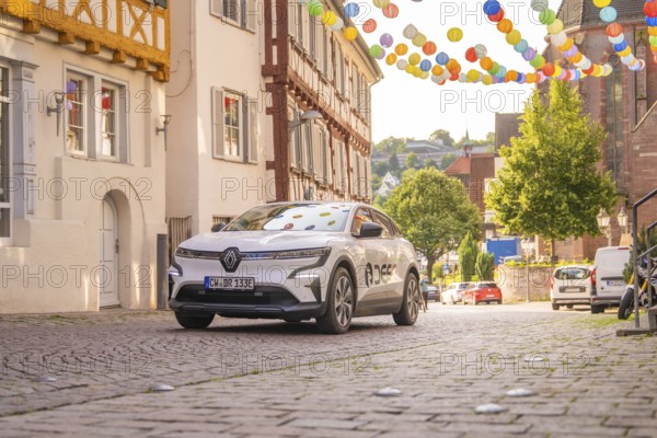 Car drives through a narrow alley, decorated with colourful lanterns, half-timbered architecture visible, Deer E, car sharing, electric car, Calw, Black Forest