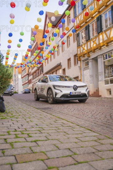 A car drives under colourful garlands in a cobbled street, Deer E, car sharing, electric car, Calw, Black Forest