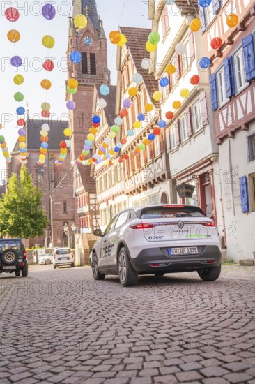 A car drives through a colourfully decorated old town with a church in the background, Deer E, car sharing, electric car, Calw, Black Forest