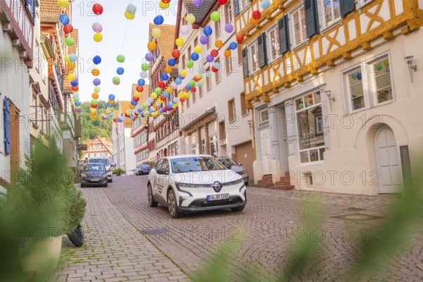 A car drives through a street decorated with colourful garlands in an old town, Deer E, car sharing, electric car, Calw, Black Forest