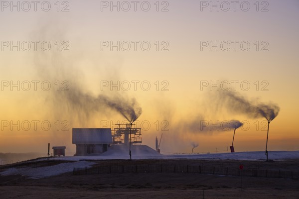 Snow cannons blow clouds of smoke on a hilltop under the purple twilight sky, winter, Route de Cretes, Hohneck, La Bresse, Vosges, France