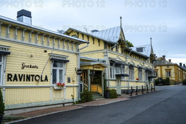 Yellow restaurant building with decorative wooden design, located on a quiet street, conveys cosiness, Naanatali, Varsinais-Suomi, Finland