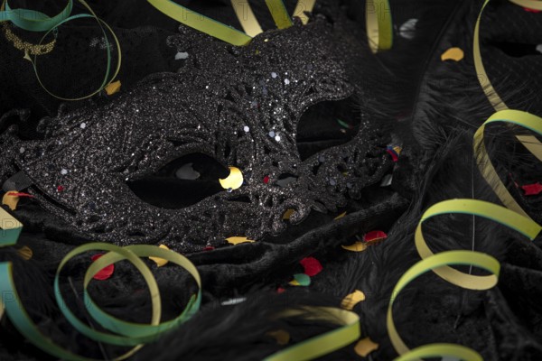 Black carnival mask with colorful confetti and streamers on dark fabric