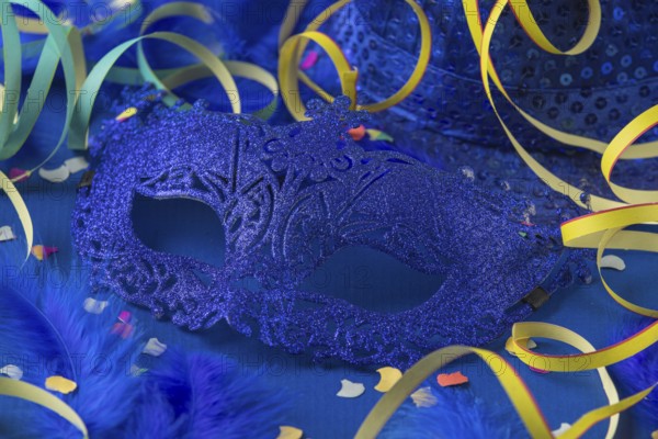 Blue mask with feathers, confetti, streamers and hat on blue background, carnival