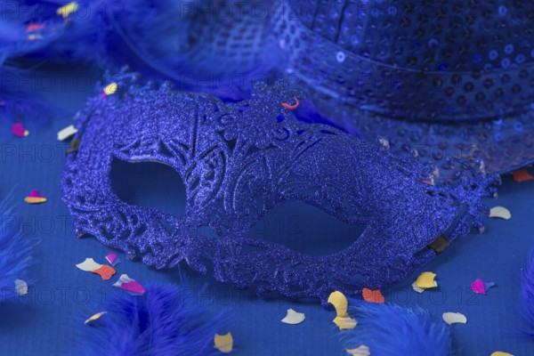 Blue mask with feathers, confetti and hat on blue background, carnival