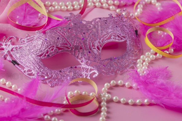 Glittering pink mask with pearls, feathers and colorful streamers on pink background, carnival