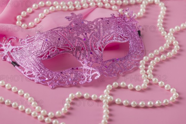 Glittering pink mask with pearl jewelry on a pink fabric