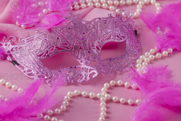 Glittering pink mask on pink background with feathers and pearl necklaces