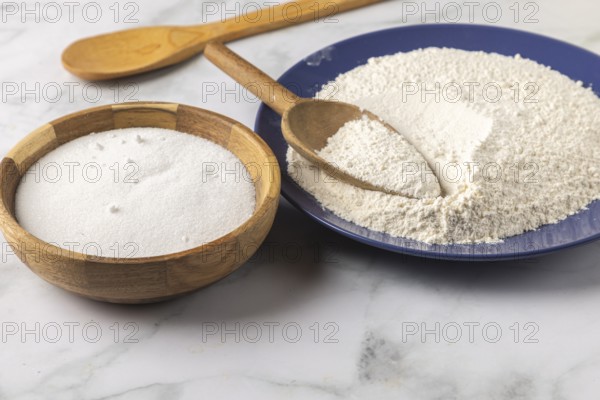 Flour and sugar in bowls with a wooden spoon on a marble plate