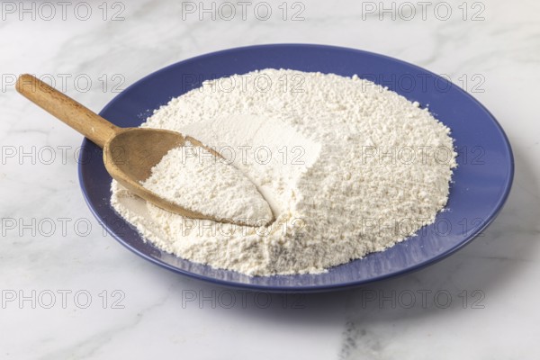 A blue plate with a large amount of flour and a wooden spoon