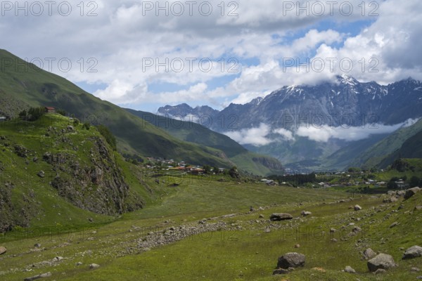 A wide valley stretches against snow-capped mountain peaks under a cloudy sky, Kazbegi, Qasbegi, Stepantsminda, Georgian Military Highway, Mtskheta-Mtianeti province, Mount Shani in the background, located in Ingushetia, Russia, High Caucasus, Georgia