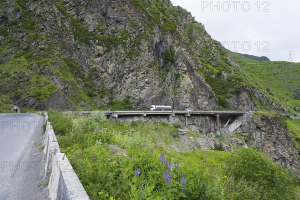 A truck crosses a bridge along steep rock faces in a green mountain landscape, damaged concrete road patched with iron pipes, Kazbegi, Stepantsminda, Georgian Military Highway, Mtskheta-Mtianeti Province, High Caucasus, Georgia