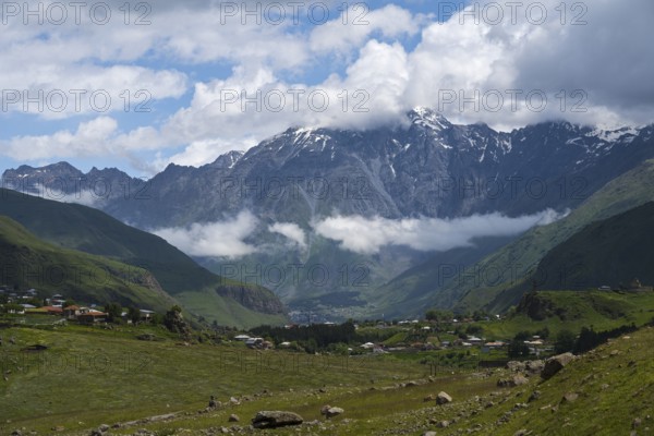 Impressive snow-capped mountains rise above a green valley with clouds in the sky, Kazbegi, Qasbegi, Stepantsminda, Georgian Military Highway, Mtskheta-Mtianeti province, Mount Shani in the background, located in Ingushetia, Russia, High Caucasus, Georgia