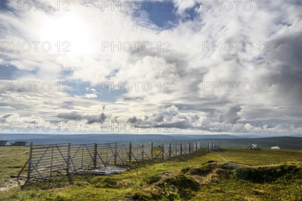 Landscape with vast sky and clouds bounded by a protective fence against snowdrifts Wooden fence along an open area, Kaunispää Caabuaivas, Lapland, Finland