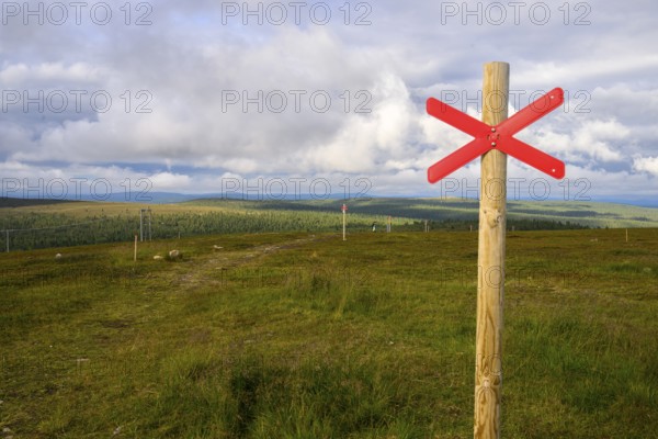 Red snowmobile snowscooter marker on a wooden post in front of a vast landscape under clouds, Kaunispää Caabuaivas, Lapland, Finland