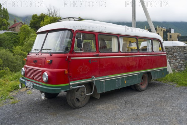 Red retro bus with green stripes on a road in a rural mountain landscape, vintage car, Robor LO 3000 bus from the GDR, Georgia