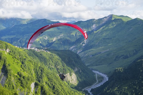 A paraglider floats over a lush green gorge with a winding river, paraglider, paraglider near Gudauri, White Aragvi River, Mtskheta-Mtianeti region, Georgian Military Highway, High Caucasus, Georgia