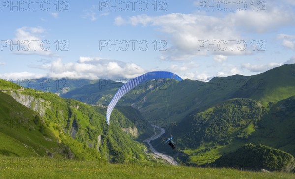 A paraglider soars over a green landscape with wide sky and valley views, paraglider, paraglider near Gudauri, White Aragvi River, Mtskheta-Mtianeti region, Georgian Military Route, High Caucasus, Georgia