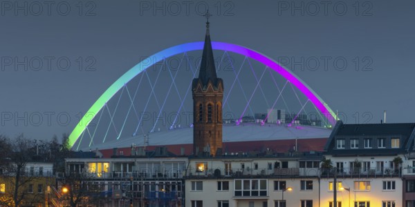 Evening view of residential buildings on the banks of the Rhine, behind them the church tower of St. John's Church and the rainbow illuminated arch of the Lanxess Arena, Cologne-Deutz, Cologne, North Rhine-Westphalia, Germany