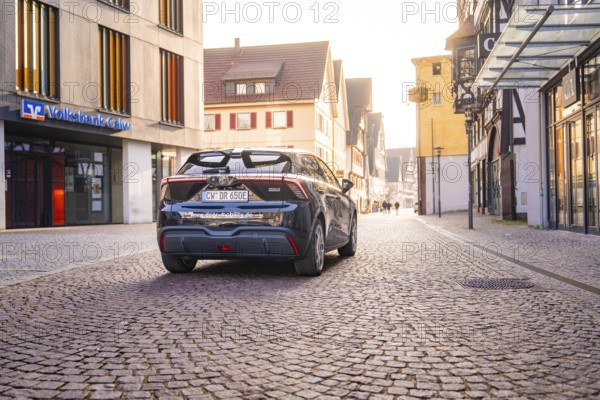 Car parked in a quiet old town with cobblestones and old buildings in diffuse light, MG4 electric car, Deer e-Carsharing, Calw, Germany