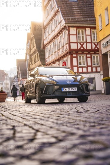 Car drives through an old town with half-timbered houses, some people on foot, MG4 electric car, deer e-car sharing, Calw, Germany
