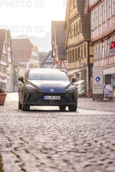 Black car drives through an old town with half-timbered houses and cobblestones, MG4 electric car, deer e-car sharing, Calw, Germany