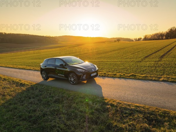 Black car on a dirt road at sunset, wide landscape in the background, MG4 electric car, deer e-car sharing, Calw, Germany