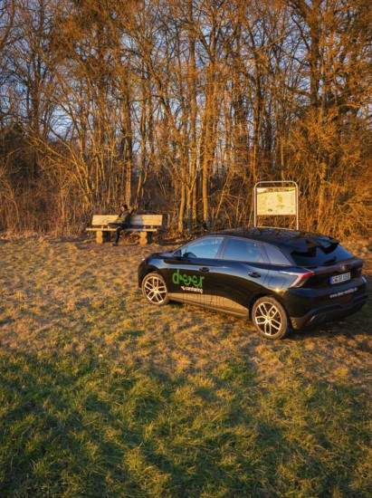 Black car parked on the edge of a forest next to a bench at sunset, MG4 electric car, deer e-car sharing, Calw, Germany
