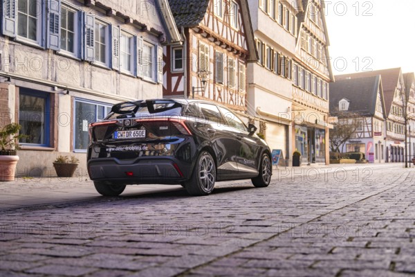 Car standing in front of half-timbered houses in a paved old town street under soft light, MG4 electric car, Deer e-Carsharing, Calw, Germany