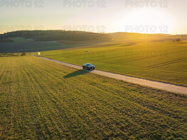 Small car on a country road surrounded by vast fields and an impressive sunset, MG4 electric car, Deer e-Carsharing, Calw, Germany