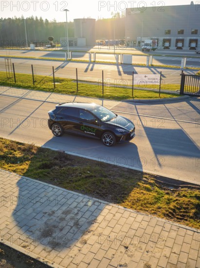 Black car driving on a paved road surrounded by a modern building landscape at sunset, MG4 electric car, deer e-car sharing, Calw, Germany