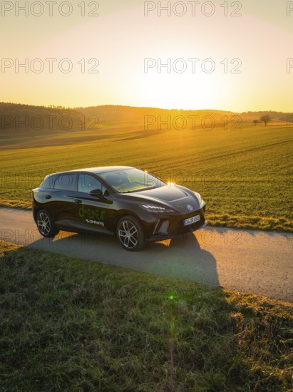 Black car in a quiet rural setting at sunset, surrounded by green fields, MG4 electric car, Deer e-Carsharing, Calw, Germany