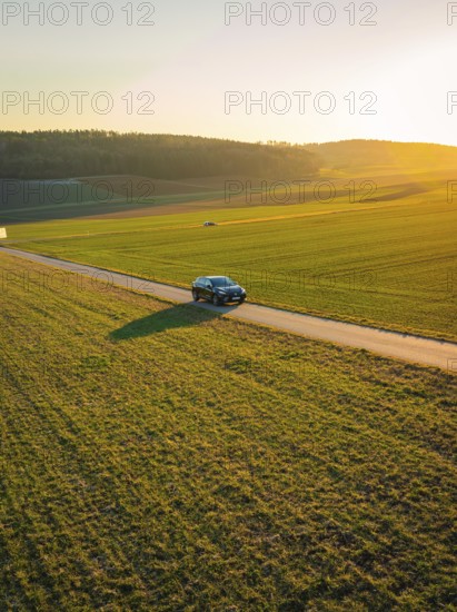 Car on a secluded country road in the middle of extensive fields with low sun in the background, MG4 electric car, Deer e-Carsharing, Calw, Germany