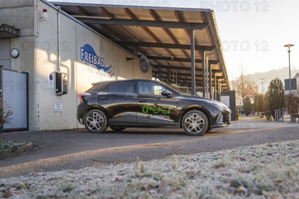 Car parked in a frosty parking lot in front of an outdoor pool building early in the morning, MG4 electric car, Deer e-Carsharing, Calw, Germany