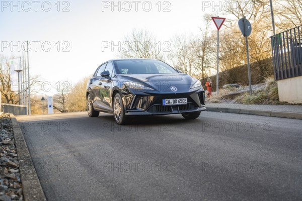 A black car at a junction surrounded by trees and road signs in sunlight, MG4 electric car, Deer e-Carsharing, Calw, Germany