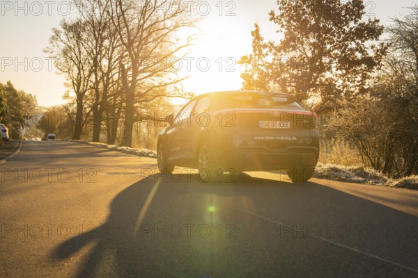 Vehicle driving on a road in atmospheric evening sunlight and casting shadows, MG4 electric car, deer e-car sharing, Calw, Germany
