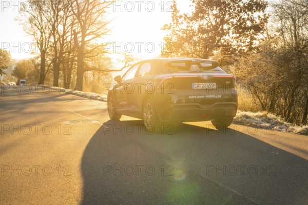 Car moving on a quiet path surrounded by trees at sunset, MG4 electric car, Deer e-Carsharing, Calw, Germany
