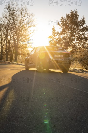 Car drives on a road under a dramatic sunset, casts long shadows, MG4 electric car, deer e-car sharing, Calw, Germany