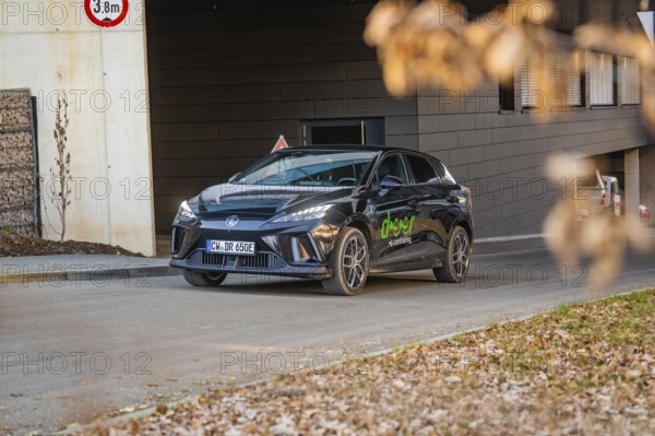 Car parked near a modern building, autumnal atmosphere due to falling leaves, MG4 electric car, deer e-car sharing, Calw, Germany