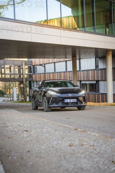 Black car passes under a modern building, stylish architecture accentuates the urban background, MG4 electric car, deer e-car sharing, Calw, Germany