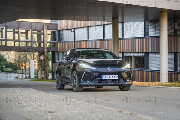 Black car on an urban road in front of a modern building at sunset, MG4 electric car, Deer e-Carsharing, Calw, Germany