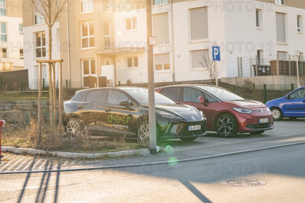 Two electric cars in a parking lot in front of residential buildings, in the warm light of the setting sun, MG4 electric car, Deer E-Carsharing, Calw, Germany