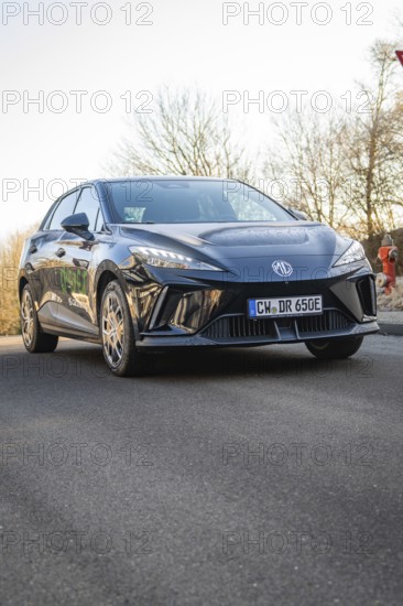 Car drives across tree-lined road, modern design reflected in sunshine, MG4 electric car, deer e-car sharing, Calw, Germany