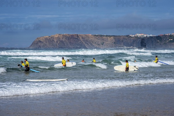 Participants in a surfing course go into the water, beach Praia de Vale Figueiras, village Arrifana in the back, western Algarve, Portugal