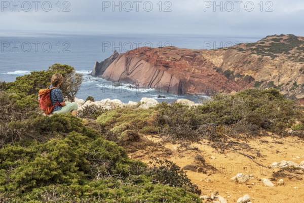 Hiking woman takes a break, view over cliff, Fishermens Trail, Rosa Vicentina, western Algarve just north of cape Cabo de Sao Vicente, Portugal