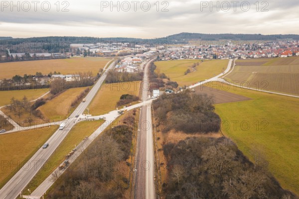 Wide fields and village settlement along a railway line under cloudy sky, tamping machine used at the Hermann Hessebahn construction site, Calw, Germany